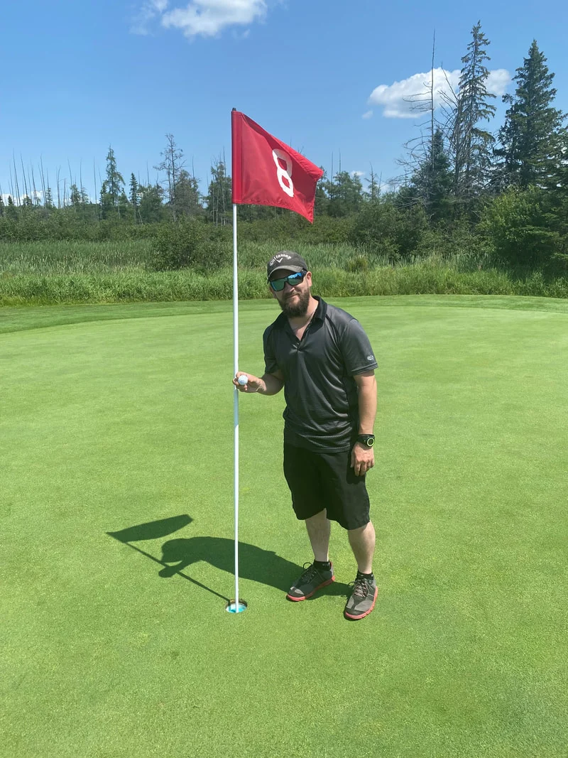 Person standing beside a flag on a golf green